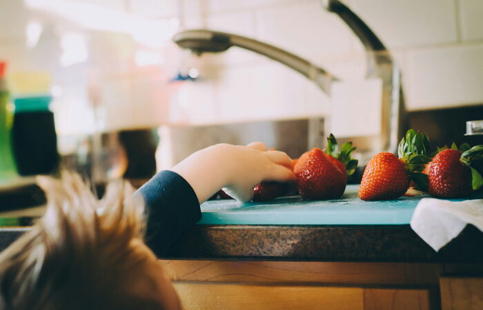 Boy getting strawberry on a kitchen counter