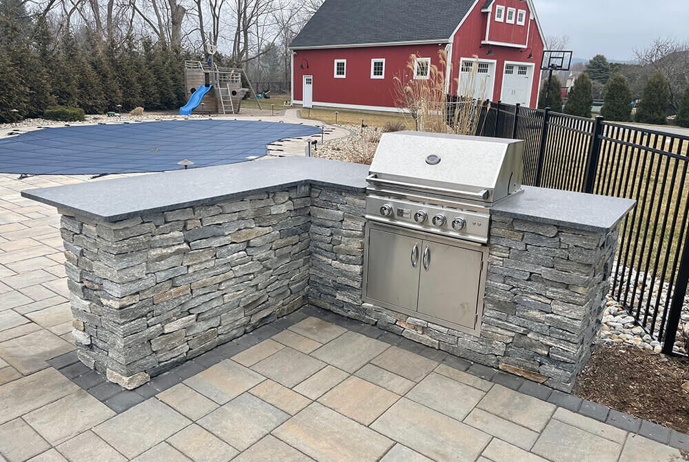 outdoor kitchen with stone facade and stainless steel integrated grill near pool