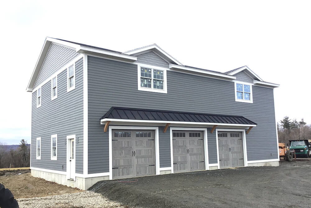 two story gray detached garage with three gray garage bay doors